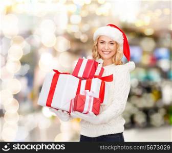 happiness, winter holidays, christmas and people concept - smiling young woman in santa helper hat with gifts over lights background