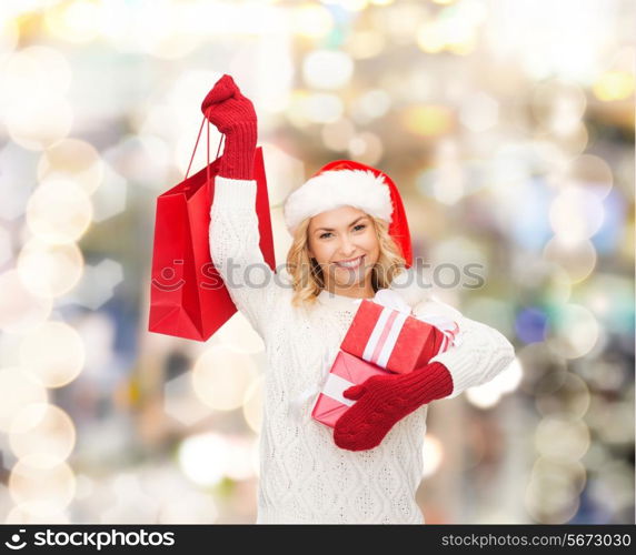 happiness, winter holidays, christmas and people concept - smiling young woman in santa helper hat with gifts and shopping bag over lights background