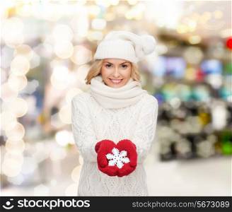 happiness, winter holidays, christmas and people concept - smiling young woman in hat, scarf and mittens holding snowflake decoration over lights background