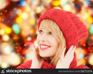 happiness, winter holidays, christmas and people concept - smiling young woman in hat and scarf over red lights background