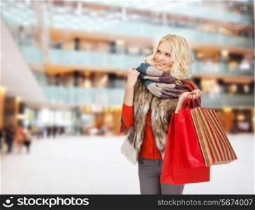 happiness, winter holidays, christmas and people concept - smiling young woman in winter clothes with red bags over shopping center background