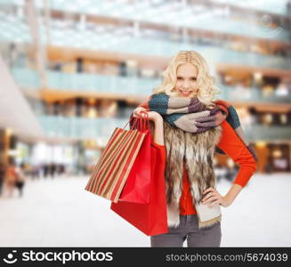 happiness, winter holidays, christmas and people concept - smiling young woman in winter clothes with red bags over shopping center background