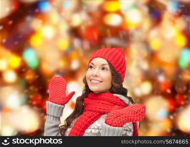 happiness, winter holidays, christmas and people concept - smiling young woman in red hat, scarf and mittens over red lights background