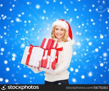 happiness, winter holidays, christmas and people concept - smiling young woman in santa helper hat with gifts over blue snowing background