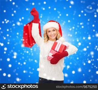 happiness, winter holidays, christmas and people concept - smiling young woman in santa helper hat with gifts and shopping bag over blue snowing background