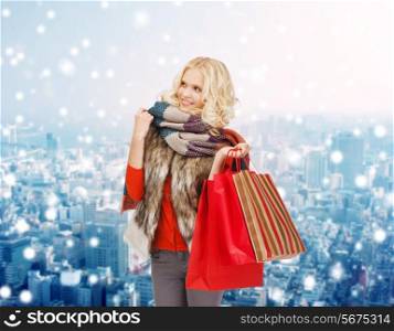happiness, winter holidays, christmas and people concept - smiling young woman in winter clothes with red shopping bags over snowy city background
