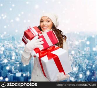 happiness, winter holidays, christmas and people concept - smiling young woman in santa helper hat with gifts over snowy city background