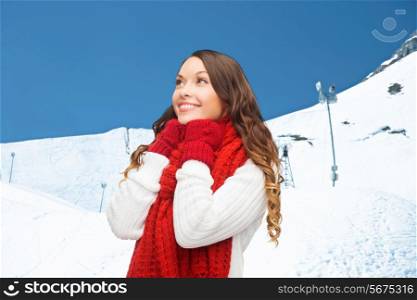 happiness, winter holidays, christmas and people concept - smiling young woman in red scarf and mittens over blue snowy background