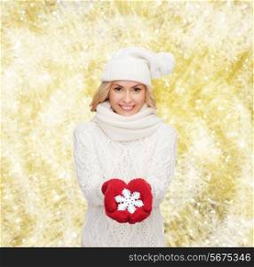 happiness, winter holidays, christmas and people concept - smiling young woman in hat, scarf and mittens holding snowflake decoration over yellow lights background