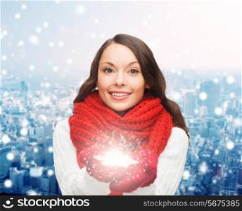 happiness, winter holidays, christmas and people concept - smiling young woman in red scarf and mittens holding snowflake over city background