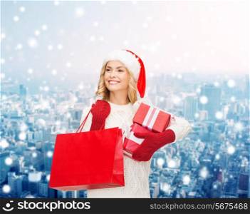 happiness, winter holidays, christmas and people concept - smiling young woman in santa helper hat with gift boxes and shopping bag over snowy city background