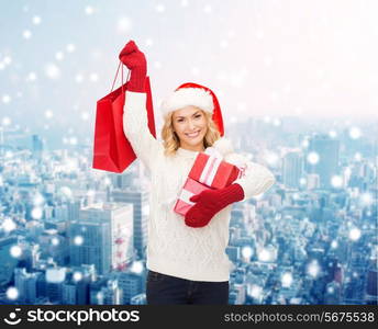 happiness, winter holidays, christmas and people concept - smiling young woman in santa helper hat with gifts and shopping bag over snowy city background