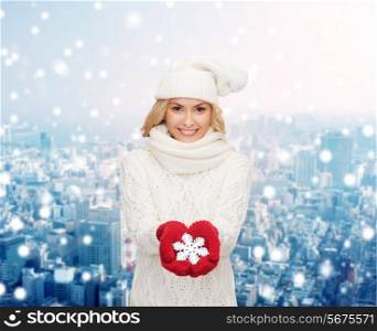 happiness, winter holidays, christmas and people concept - smiling young woman in hat, scarf and mittens holding snowflake decoration over snowy city background