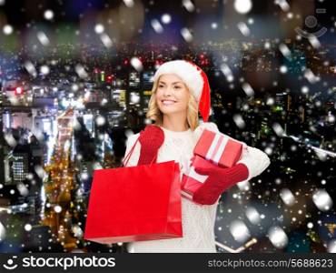 happiness, winter holidays, christmas and people concept - smiling young woman in santa helper hat with gift boxes and shopping bag over snowy night city background