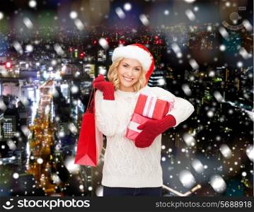 happiness, winter holidays, christmas and people concept - smiling young woman in santa helper hat with gifts and shopping bag over snowy night city background