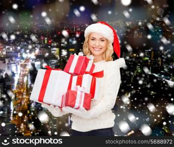 happiness, winter holidays, christmas and people concept - smiling young woman in santa helper hat with gifts over snowy night city background