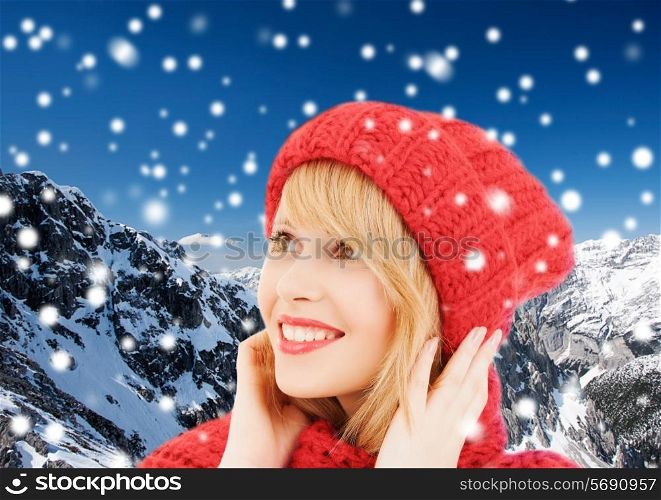 happiness, winter holidays, christmas and people concept - smiling young woman in red hat and scarf over blue snowy background