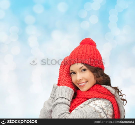 happiness, winter holidays, christmas and people concept - smiling young woman in red hat, scarf and mittens over blue lights background