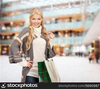 happiness, winter holidays, christmas and people concept - smiling young woman in winter clothes with bags over shopping center background