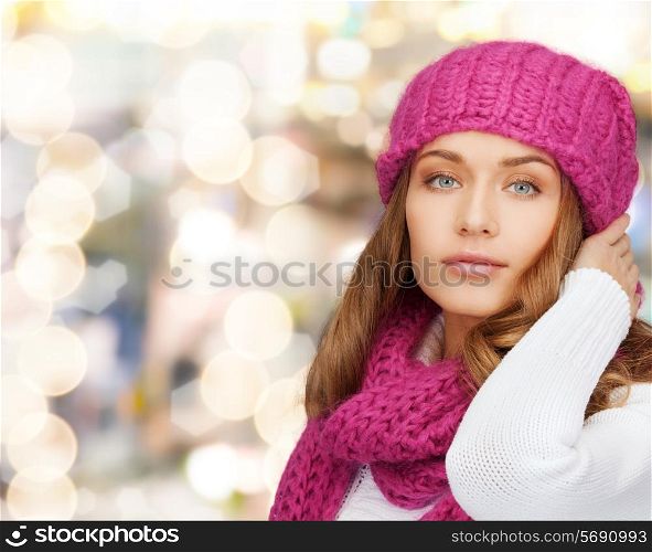 happiness, winter holidays, christmas and people concept - smiling young woman in pink hat and scarf over lights background