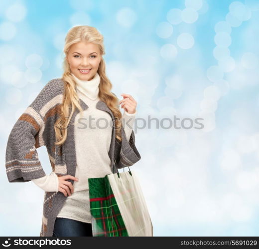 happiness, winter holidays, christmas and people concept - smiling young woman in winter clothes with shopping bags over blue lights background