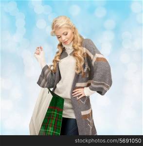 happiness, winter holidays, christmas and people concept - smiling young woman in winter clothes with shopping bags over blue lights background