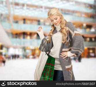 happiness, winter holidays, christmas and people concept - smiling young woman in winter clothes with bags over shopping center background