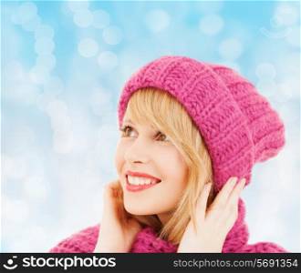 happiness, winter holidays, christmas and people concept - smiling young woman in pink hat and scarf over blue lights background
