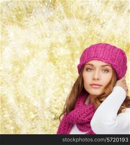 happiness, winter holidays, christmas and people concept - smiling young woman in pink hat and scarf over yellow lights background