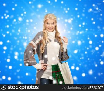 happiness, winter holidays, christmas and people concept - smiling young woman in winter clothes with shopping bags over blue snowy background