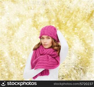 happiness, winter holidays, christmas and people concept - smiling young woman in pink hat and scarf over yellow lights background