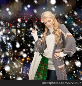 happiness, winter holidays, christmas and people concept - smiling young woman in winter clothes with shopping bags over snowy city background