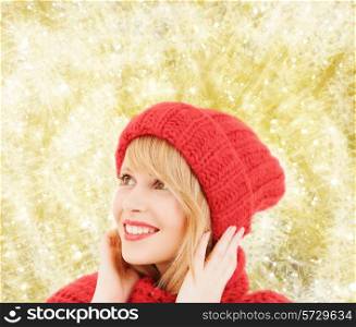 happiness, winter holidays, christmas and people concept - smiling young woman in red hat and scarf over yellow lights background