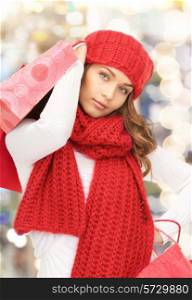 happiness, winter holidays, christmas and people concept - smiling young woman in hat and scarf with shopping bags over lights background