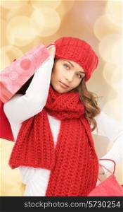 happiness, winter holidays, christmas and people concept - smiling young woman in hat and scarf with shopping bags over beige lights background
