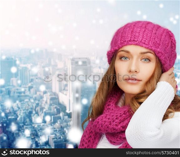 happiness, winter holidays, christmas and people concept - smiling young woman in pink hat and scarf over snowy city background