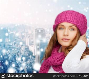 happiness, winter holidays, christmas and people concept - smiling young woman in pink hat and scarf over snowy city background