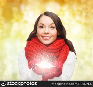happiness, winter holidays, christmas and people concept - smiling young woman in red scarf and mittens holding snowflake over yello lights background