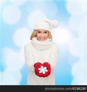 happiness, winter holidays, christmas and people concept - smiling young woman in hat, scarf and mittens holding snowflake decoration over blue lights background