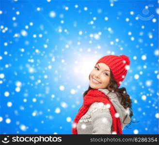 happiness, winter holidays, christmas and people concept - smiling young woman in red hat and scarf over blue snowy background