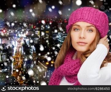 happiness, winter holidays, christmas and people concept - smiling young woman in pink hat and scarf over snowy night city background