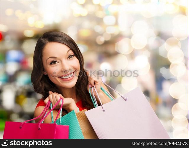 happiness, winter holidays, christmas and people concept - smiling young woman with shopping bags over lights background