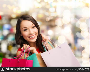 happiness, winter holidays, christmas and people concept - smiling young woman with shopping bags over lights background