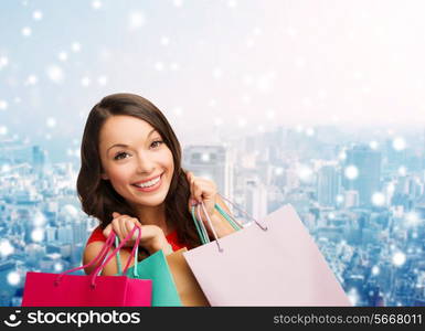 happiness, winter holidays, christmas and people concept - smiling young woman with shopping bags over snowy city background