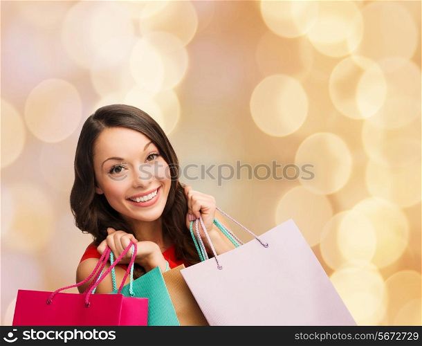 happiness, winter holidays, christmas and people concept - smiling young woman with shopping bags over beige lights background