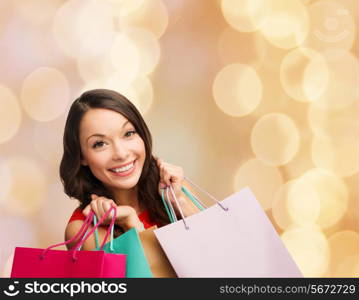 happiness, winter holidays, christmas and people concept - smiling young woman with shopping bags over beige lights background