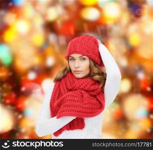 happiness, winter holidays, christmas and people concept - young woman in hat and scarf over red lights background