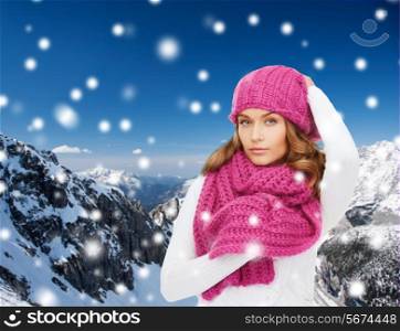 happiness, winter holidays, christmas and people concept - young woman in pink hat and scarf over snowy mountains background
