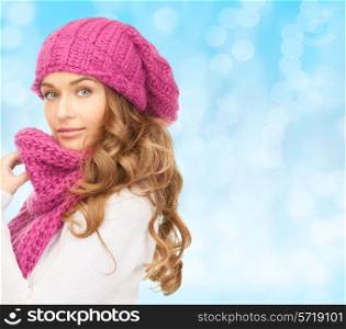 happiness, winter holidays, christmas and people concept - young woman in pink hat and scarf over blue lights background