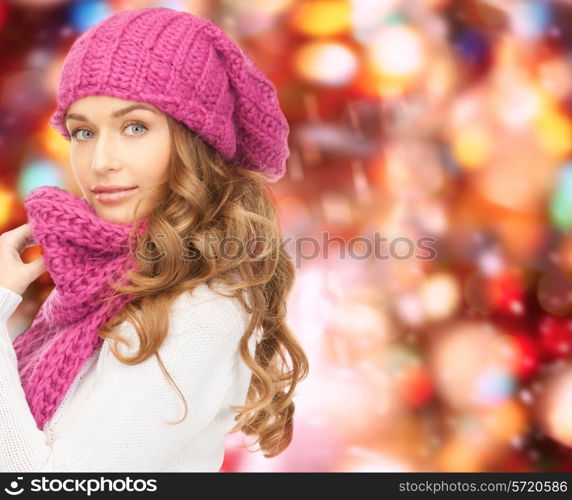 happiness, winter holidays, christmas and people concept - young woman in pink hat and scarf over red lights background